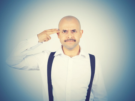 Bald crazy mad man in wihte shirt with a finger to his temple like a gunの写真素材