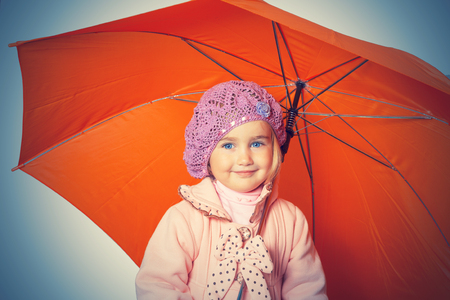 Little cute girl with an orange umbrella isolated on white background の写真素材