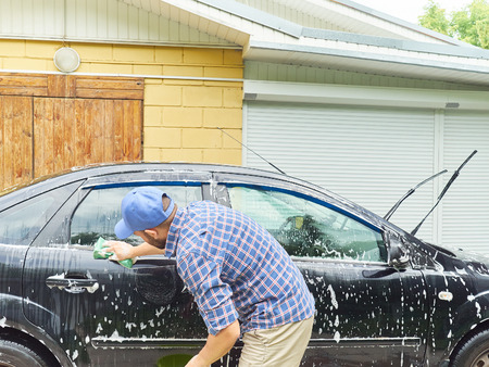 Young man washing his black car near the houseの写真素材