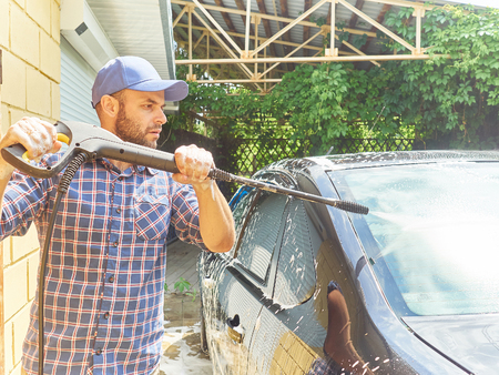 Young man washing his black car near the houseの写真素材