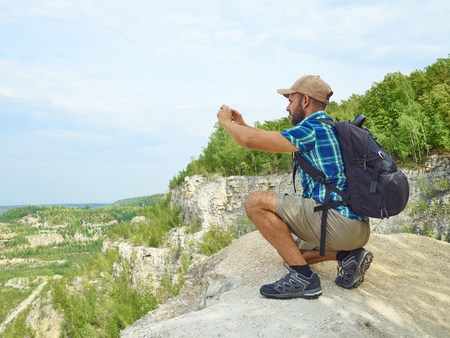 Man Tourist is Using a Smartphone While Sitting on the Edge of a Cliff In the Mountains.の写真素材