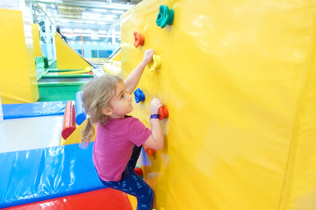 Little Girl Climbing a Rock Wall Indoor. Children's Entertainment Sports Soft Ground. の写真素材