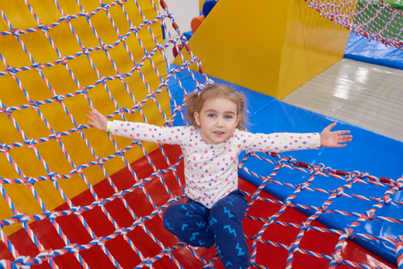 Girl swinging on the Hammock Ropes Course with Long Fair Hair in Indoors Playground. Active Toddler Girl Having Fun At Sport Centerの写真素材