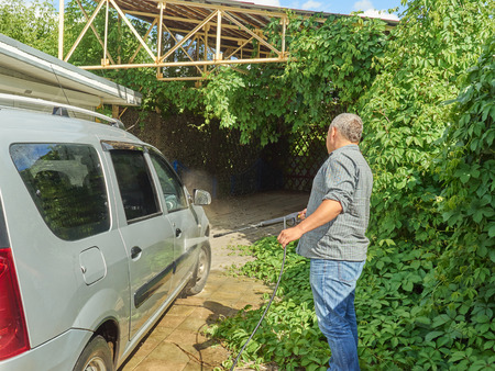 Man washing his silver car near the house.の写真素材