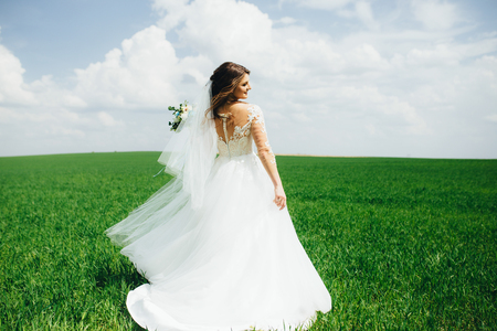 Wonderful happy bride spinning in the field while walking. Carrying her wedding bouquet and smiling. Great embroidery on the dress.の写真素材