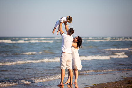 Young happy family walking along the seashore at the day time. Father flips up his boy.の写真素材