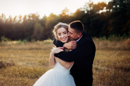 Great portrait of a wedding couple, which is walking in the field. A groom embracing his bride behind and she is embracing him and smiling.の写真素材