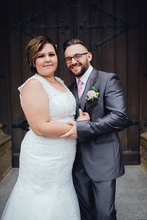 Portrait of a beautiful wedding couple. They are standing near an old building, embracing each other, looking at the camera and smiling.の写真素材