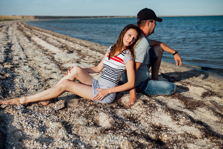 Portrait of a young happy family. Husband and wife sitting back to back on the beach. A woman is looking at the camera and smiling.の写真素材