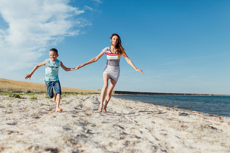 Funny portrait of a happy family on the beach. Mother is holding his son by the hand, they are running on the seashore, looking at the camera and smiling.の写真素材