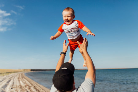 Funny portrait of a father and son, while they are playing on the beach. Father is holding his boy...
