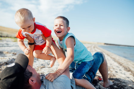 Funny portrait of a father and his sons, while they are playing on the beach, lying on the sand,...