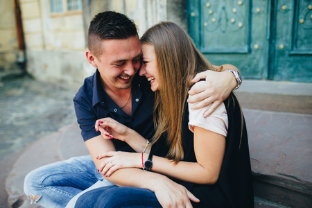 Lovely portrait of a young couple. They are sitting on the stairs, embracing and smiling.の写真素材