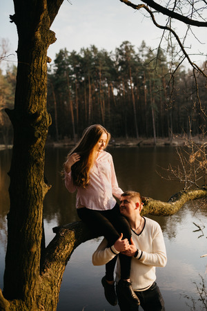 Beautiful portrait of a pregnant woman and her husband. They are standing near the river, a girl is sitting on the branch.の写真素材