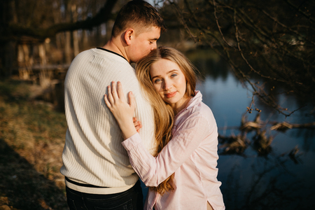 Beautiful portrait of a pregnant woman and her husband. They are standing near the river, embracing and smiling.の写真素材