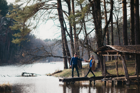 Beautiful portrait of a pregnant woman and her husband. They are walking in the forest, standing near the river, holding their hands.の写真素材