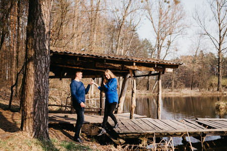 Beautiful portrait of a pregnant woman and her husband. They are walking in the forest, standing near the river, holding their hands.の写真素材