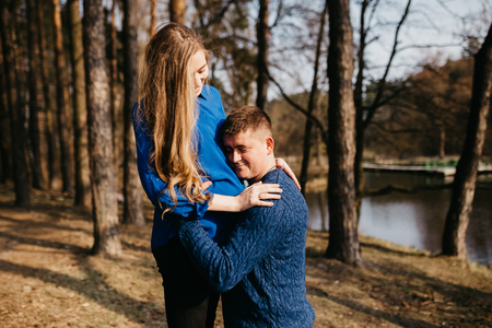 Beautiful portrait of a pregnant woman and her husband. They are walking in the forest, standing near the river. A man is embracing her tummy and smiling.の写真素材