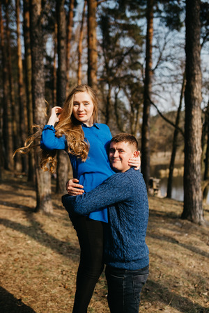 Beautiful portrait of a pregnant woman and her husband. They are walking in the forest, standing near the river. A man is embracing her tummy and smiling.の写真素材