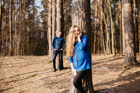 Beautiful portrait of a pregnant woman and her husband. They are walking in the forest, standing far from each other near the trees and smiling.の写真素材