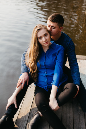 Beautiful portrait of a pregnant woman and her husband. They are walking in the forest, sitting near the river, embracing and looking at the camera.の写真素材