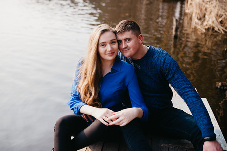 Beautiful portrait of a pregnant woman and her husband. They are walking in the forest, sitting near the river, embracing, looking at the camera and smiling.の写真素材