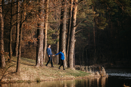 Beautiful portrait of a pregnant woman and her husband. They are walking in the forest, standing near the river, holding their hands.の写真素材