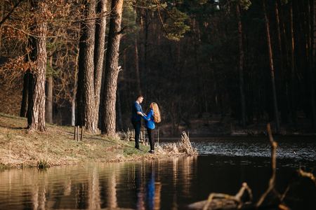Beautiful portrait of a pregnant woman and her husband. They are walking in the forest, standing near the river, embracing and looking at each other.の写真素材