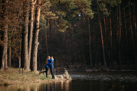 Beautiful portrait of a pregnant woman and her husband. They are walking in the forest, standing face to face near the river, embracing and looking at each other.の写真素材