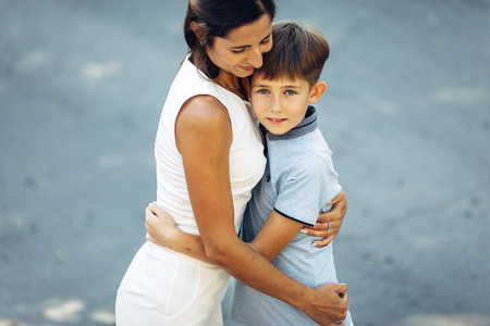 Portrait of a young happy mother and her little son. They are walking, standing on the street, embracing and smiling.の写真素材