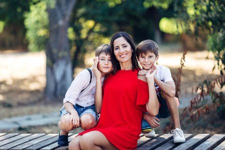 Portrait of a young beautiful woman with her son and nephew. They are sitting on the bench, embracing and smiling, looking at the camera.の写真素材