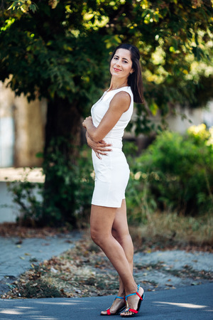 Portrait of a beautiful lady. She is standing near the trees, crossing her hands, smiling and looking at the cameraの写真素材
