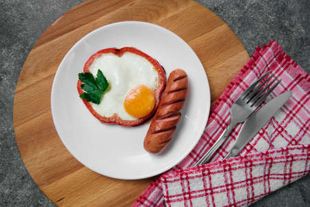 fried egg, red pepper, sausage, towel and cutlery on a dark tableの写真素材