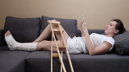 Woman in a plaster cast lies on the couch at home and using smart phone