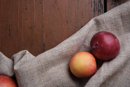 Juicy fruits in a linen tablecloth on a old wooden table. Apples, plums, apricots on a dark red background. Top view.の写真素材