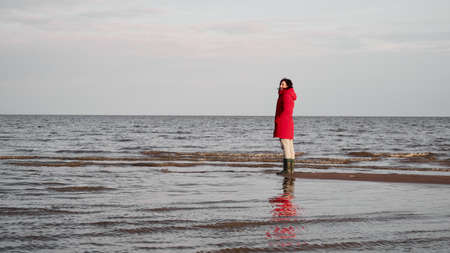 A Woman in a Red Jacket Looks at the Foamy Wavesの写真素材