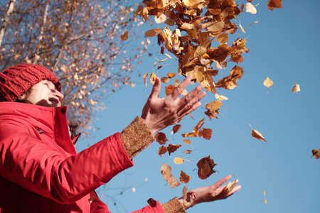 A Woman in A Red Jacket Throws Yellow Leaves. Autumn Landscape. Slow motion video.の写真素材