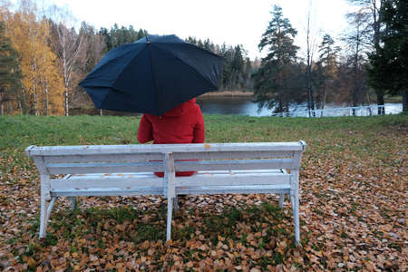 A Woman in a Red Jacket Is Sitting on a White Bench in the Park.の写真素材