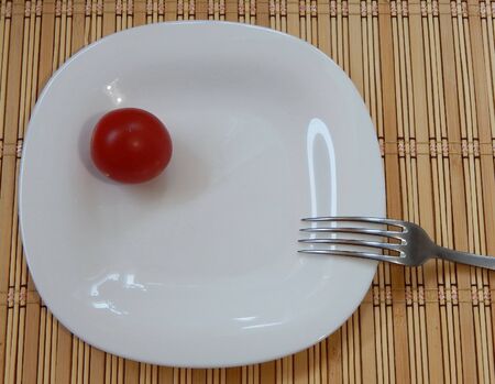 A red tomato on a white plate, part of a fork on the table.の写真素材