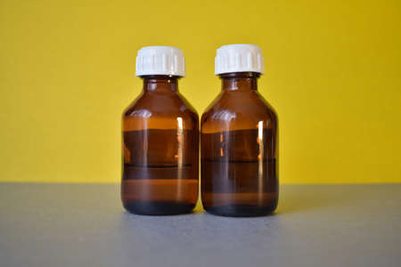Two brown cosmetic bottles with a white lid on a gray-yellow backgroundの写真素材