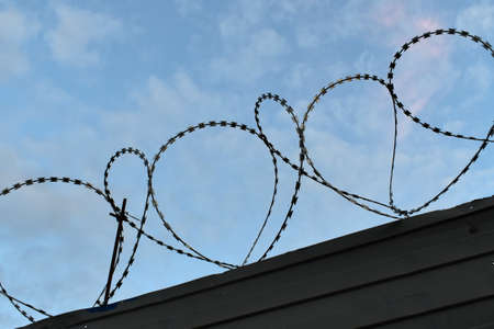 Protective barbed wire on the fence against the blue skyの写真素材