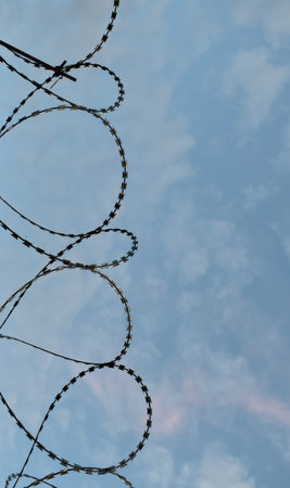 Protective barbed wire on the fence against the blue sky
