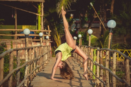Girl in green t-shirt on the bridge making acrobatic the background of a bungalowの写真素材