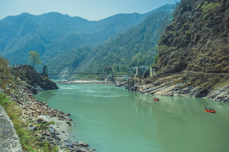 Suspension bridge across the Ganges and rafters floating downstreamの写真素材