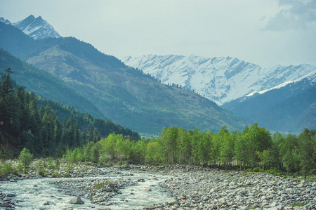 In the front: Beas river on a background himalayan snow mountains and white cloudsの写真素材