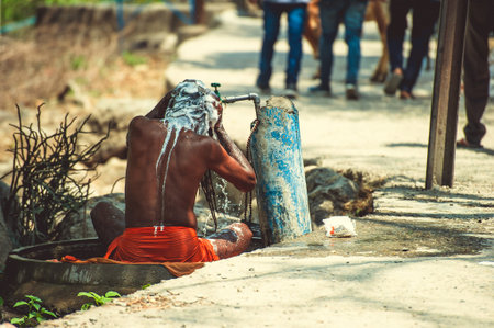 Sadhu is washed under running water near the road.