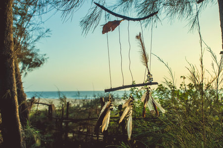 Amulet of sticks and feathers against the background of the ocean during sunset.