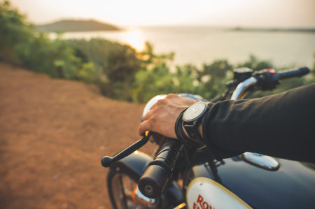 India, Goa -April 6, 2017: Man's hand with a watch on the helm of the Royal Enfield motorcycle during sunset.のeditorial素材