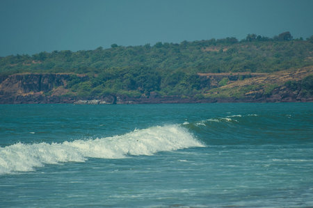 Waves of the Arabian Sea rolling on a sandy beach in the background of a rocky coast.