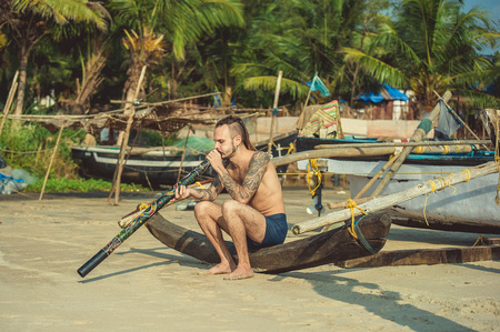 Hippies with tattoos and dreadlocks playing on the didgeridoo on the beach.のeditorial素材